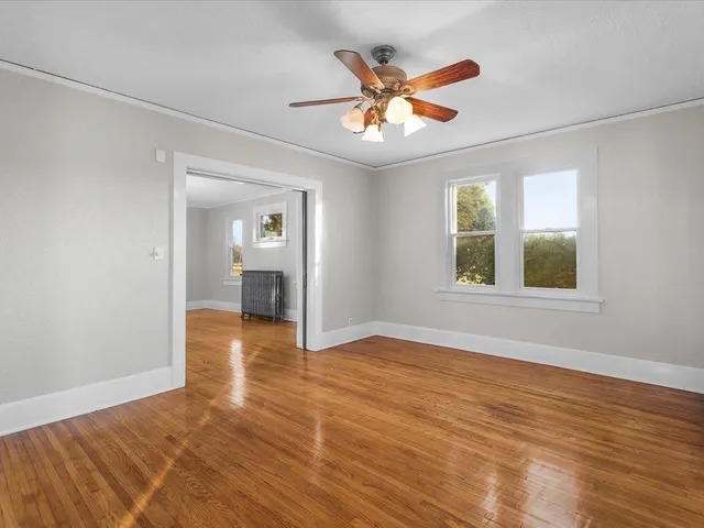 an empty room with wooden floor chandelier and windows