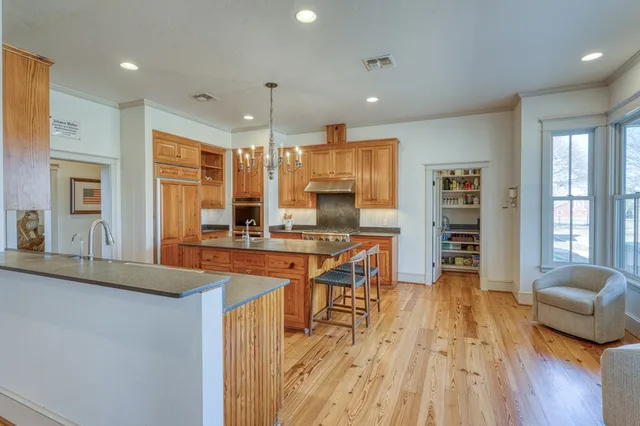 a kitchen with stainless steel appliances granite countertop a refrigerator a sink dishwasher a stove and a dining table with wooden floor