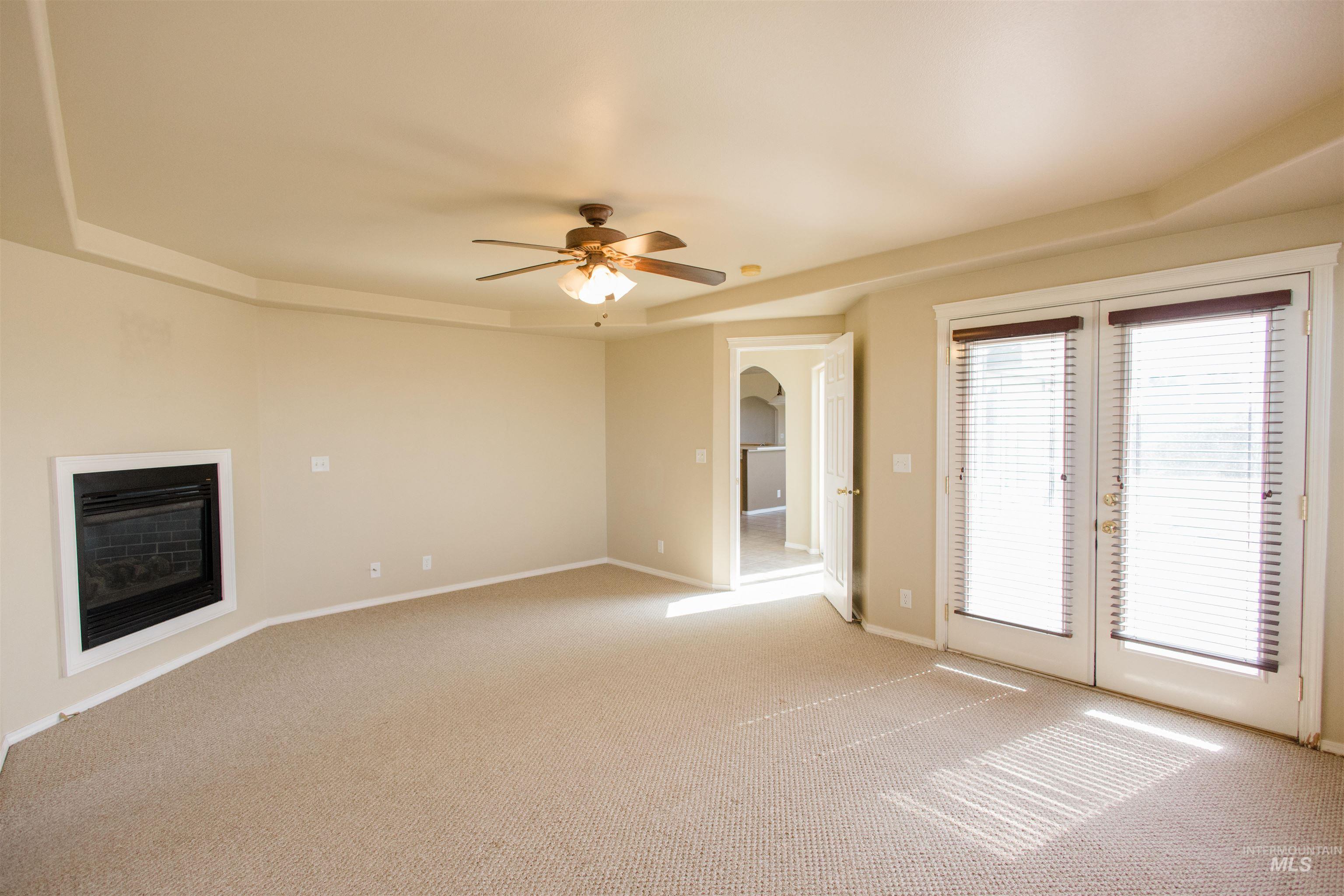 1571 Southeast Hamilton Road Mountain Home, ID 83647 - Photo 13 of 50 Unfurnished living room featuring french doors, light carpet, ceiling fan, a glass covered fireplace, and a tray ceiling