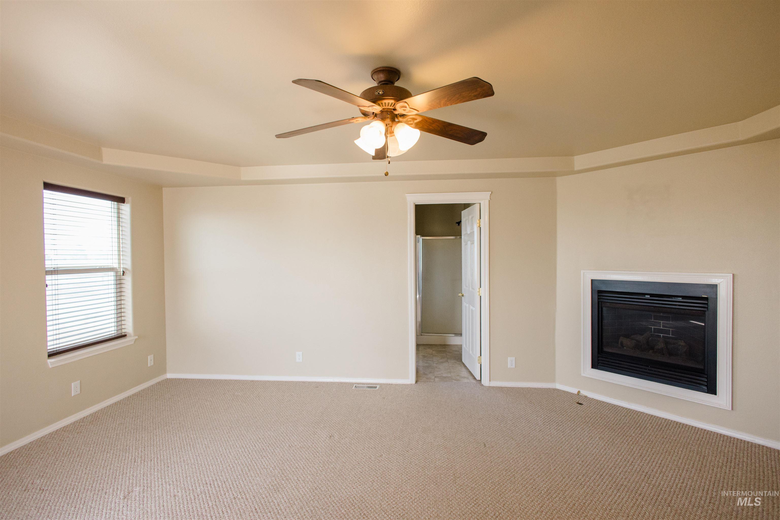 1571 Southeast Hamilton Road Mountain Home, ID 83647 - Photo 14 of 50 Unfurnished living room featuring a glass covered fireplace, light colored carpet, and ceiling fan