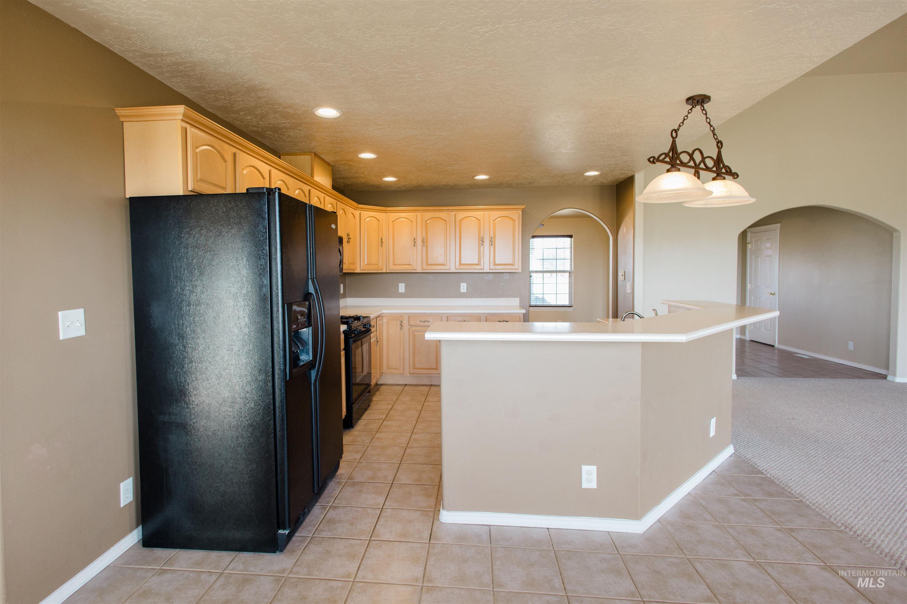 1571 Southeast Hamilton Road Mountain Home, ID 83647 - Photo 3 of 50 Kitchen with black appliances, light wood finish cabinets, light countertops, and a center island with sink