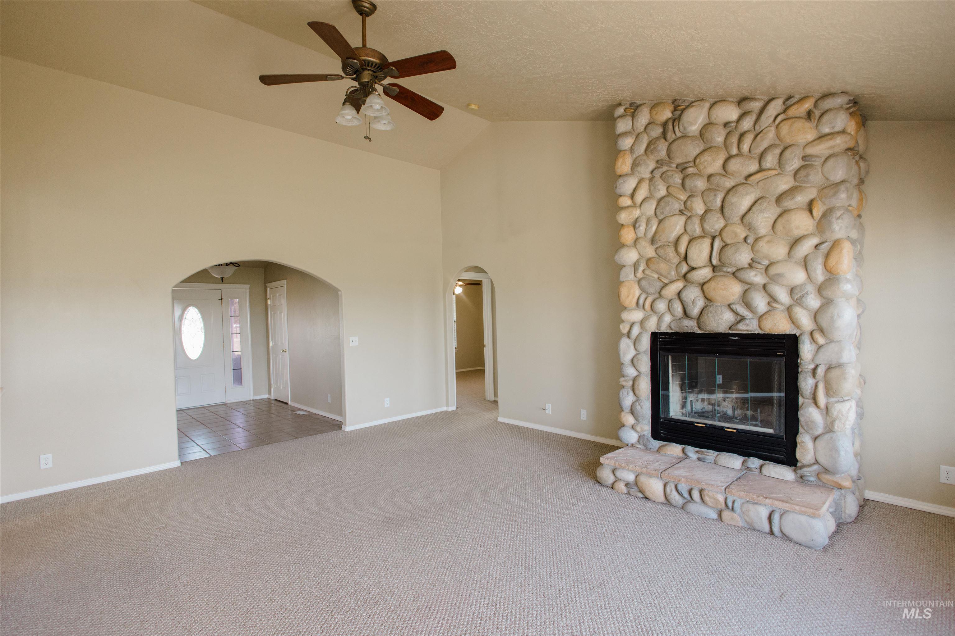 1571 Southeast Hamilton Road Mountain Home, ID 83647 - Photo 7 of 50 Unfurnished living room with a ceiling fan, light colored carpet, a fireplace, vaulted ceiling, and arched walkways