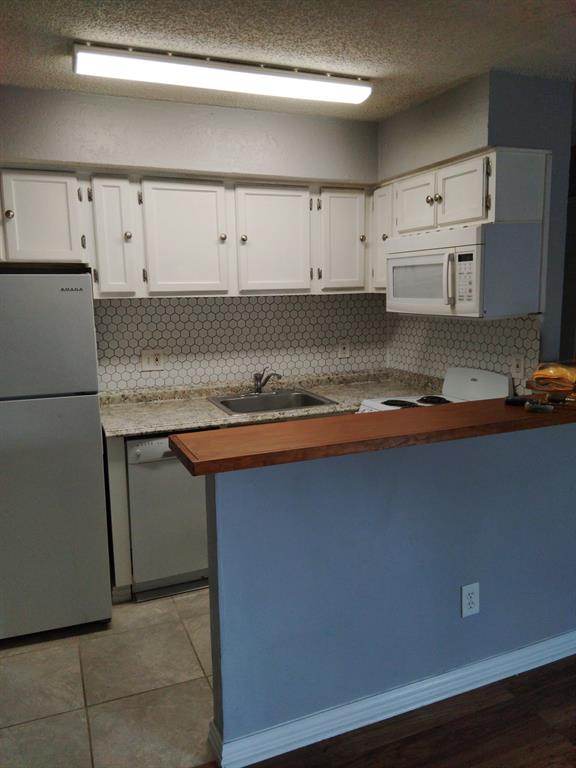 9809 Walnut Street, Unit E305 Dallas, TX 75243 - Photo 2 of 16 Kitchen featuring butcher block counters, white appliances, a peninsula, white cabinets, and tasteful backsplash