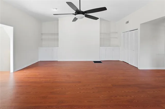 an empty room with wooden floor chandelier and windows