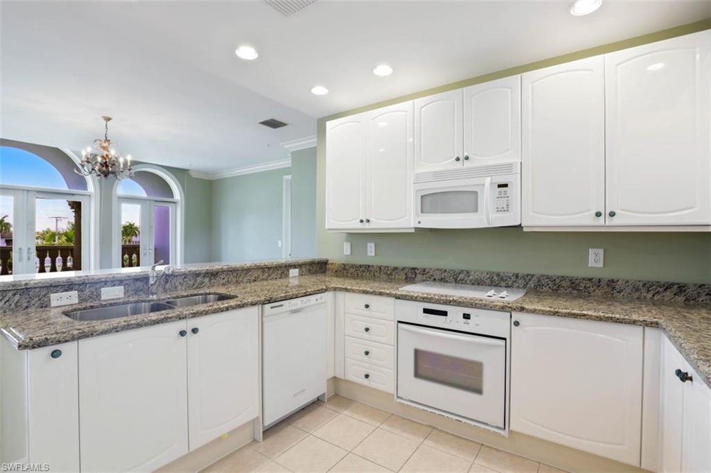 900 5th Avenue South, Unit 301 Naples, FL 34102 - Photo 6 of 17 a kitchen with granite countertop white cabinets white appliances and granite countertops with wooden floor