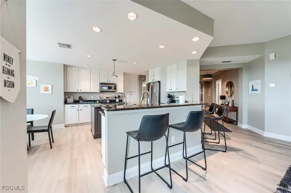 a kitchen with stainless steel appliances kitchen island granite countertop a table chairs refrigerator and microwave