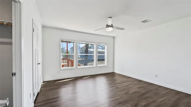 an empty room with wooden floor fan and windows