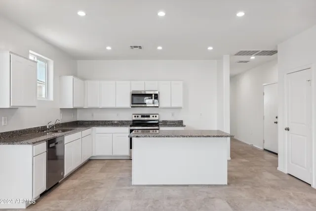 a kitchen with stainless steel appliances granite countertop a stove top oven a sink a refrigerator and white cabinets