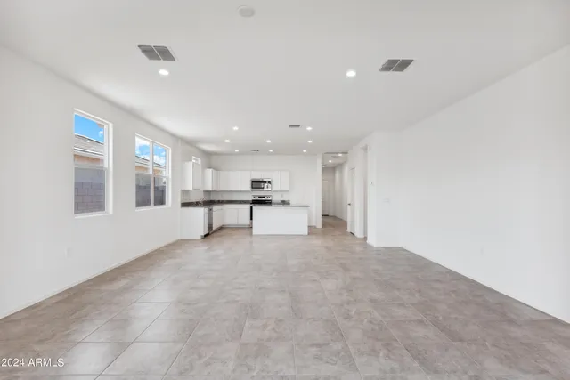 a view of an empty room with kitchen and window