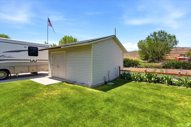 72 Canal Bank Road Garland, UT 84312 - Photo 33 of 40 Exterior storage shed with double doors and a concrete pad, situated on a grassy lawn with a wood fence bordering a garden area
