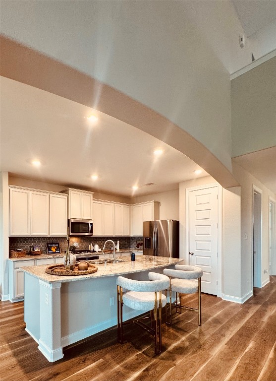 2023 Pine Ledge Road Pearland, TX 77089 - Photo 5 of 29 This modern kitchen features an open layout with high ceilings, elegant cabinetry, stainless steel appliances, and a large island with seating. The warm wood flooring adds a cozy touch.