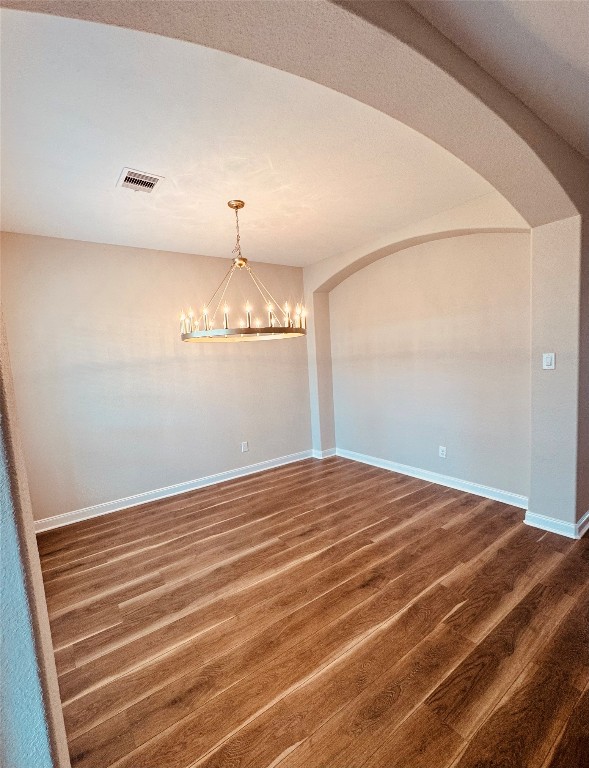 2023 Pine Ledge Road Pearland, TX 77089 - Photo 8 of 29 This photo showcases a bright, open room with warm wood flooring, soft beige walls, and an elegant chandelier. The arched entryway adds a touch of sophistication, making it ideal for a dining or living space.