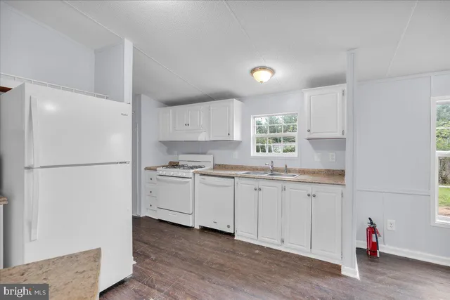 a kitchen with granite countertop white cabinets white appliances a sink and a refrigerator