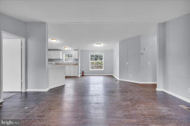 a view of an empty room with wooden floor and a kitchen