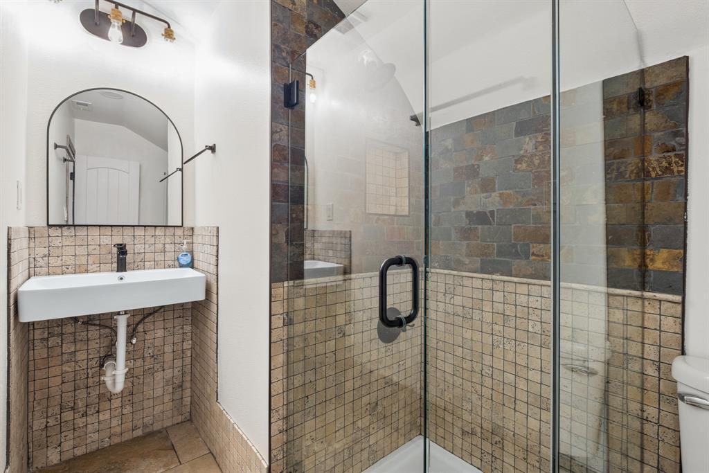 15539 Preston Road, Unit 1037 Dallas, TX 75248 - Photo 32 of 36 Glass-enclosed shower with stone tile surround, stone mosaic wall tiling, wall-mounted rectangular sink, and arched mirror