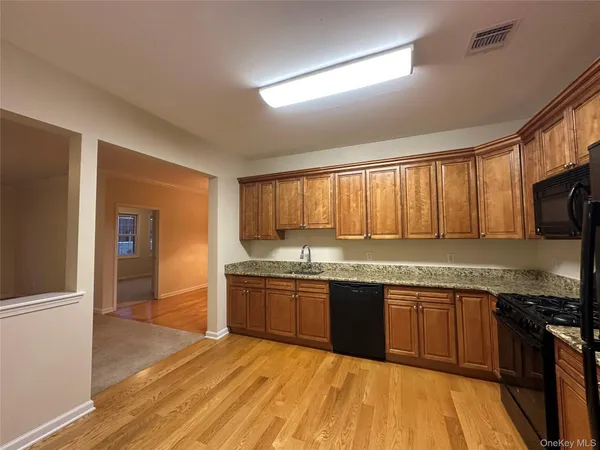 a large kitchen with granite countertop a stove top oven a sink dishwasher and wooden cabinets with wooden floor