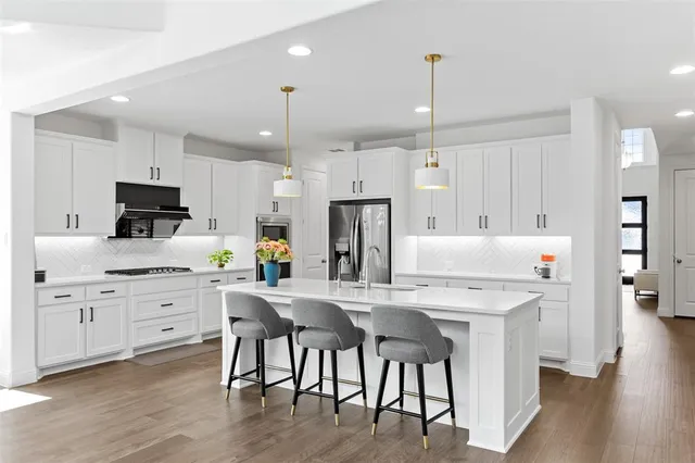 a kitchen with stainless steel appliances kitchen island granite countertop a dining table chairs refrigerator and microwave