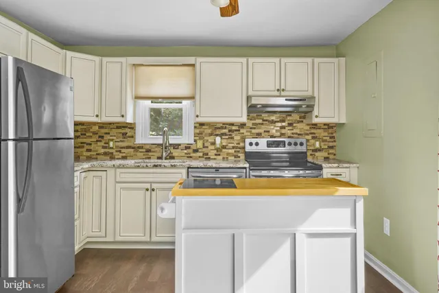 a kitchen with kitchen island a refrigerator a stove a sink and white cabinets with wooden floor