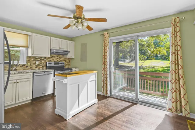 a kitchen with kitchen island granite countertop a stove a sink and white cabinets with wooden floors