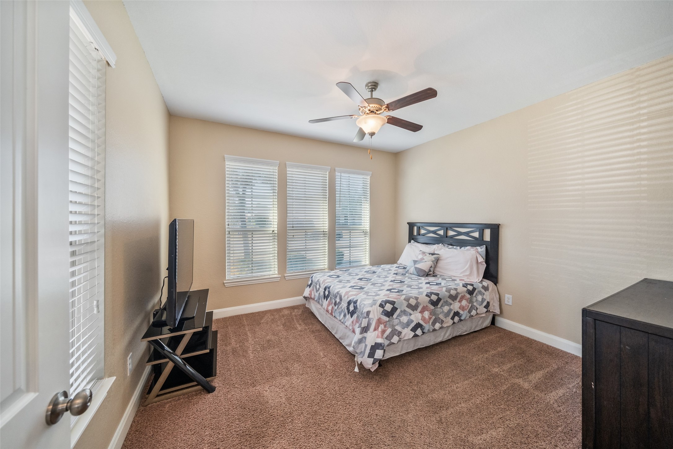 4747 Abercorn Street Rosharon, TX 77583 - Photo 31 of 46 This cozy bedroom features neutral walls, carpeted flooring, and ample natural light from large windows. It includes a ceiling fan, a comfortable bed, and a TV setup, creating a welcoming and functional space.