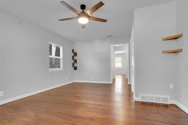 an empty room with wooden floor chandelier fan and windows