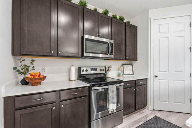 7685 Timber Country Road Eagle Mountain, UT 84005 - Photo 12 of 39 Modern kitchen featuring dark wood-finish cabinetry with silver hardware, white solid surface countertops, and stainless steel appliances