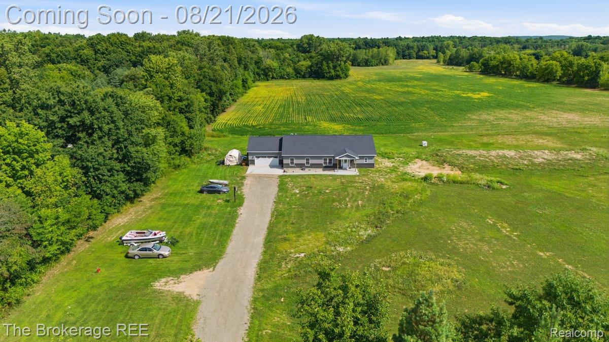 9161 East Coldwater Road Davison, MI 48423 - Photo 2 of 52 Single-story residence with a gray facade, an attached two-car garage, a gravel driveway, and surrounding expansive green fields