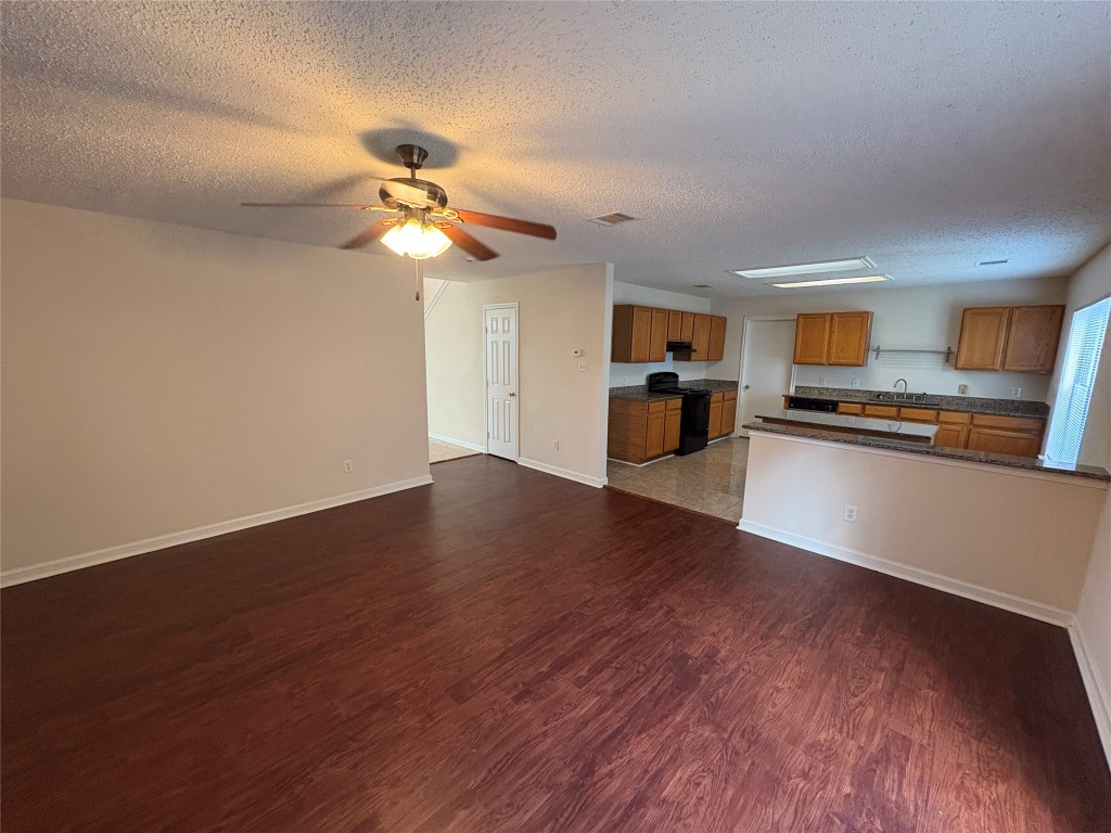 1367 Lakeside Loop Round Rock, TX 78665 - Photo 6 of 19 Kitchen featuring brown cabinetry, dark countertops, black range oven, wood finished floors, and a textured ceiling