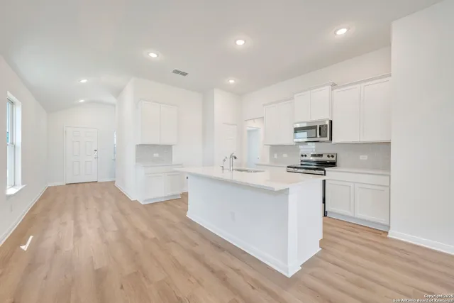 a open kitchen with white cabinets a sink dishwasher a stove and a refrigerator with wooden floor