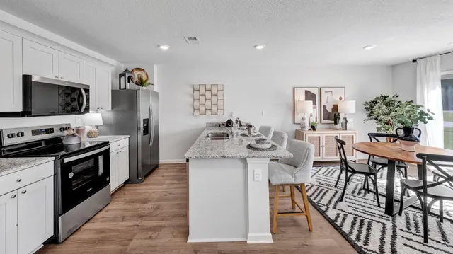 a kitchen with stainless steel appliances kitchen island granite countertop a stove top oven a sink dishwasher a dining table and chairs with wooden floor