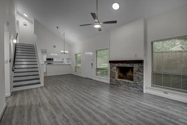 an empty room with wooden floor a ceiling fan a fireplace and windows