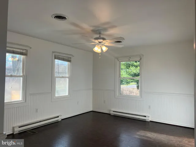 an empty room with wooden floor chandelier fan and windows