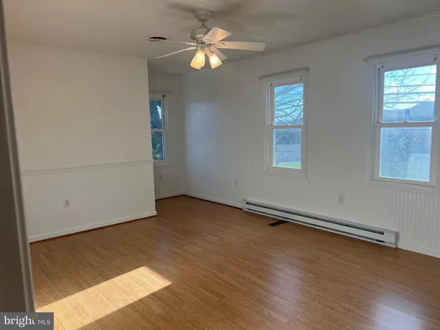 an empty room with wooden floor chandelier fan and windows