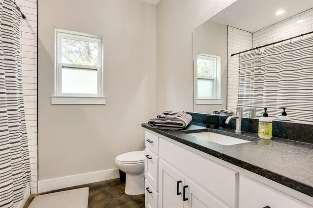 a bathroom with a granite countertop sink a toilet a mirror and a window