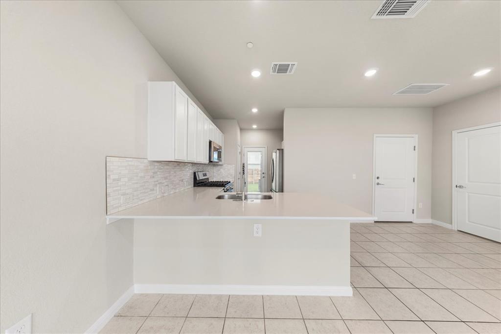 9015 Cattle Baron Path, Unit 1502 Austin, TX 78747 - Photo 21 of 32 Kitchen featuring white cabinets, stainless steel appliances, a peninsula, decorative backsplash, and light tile patterned flooring
