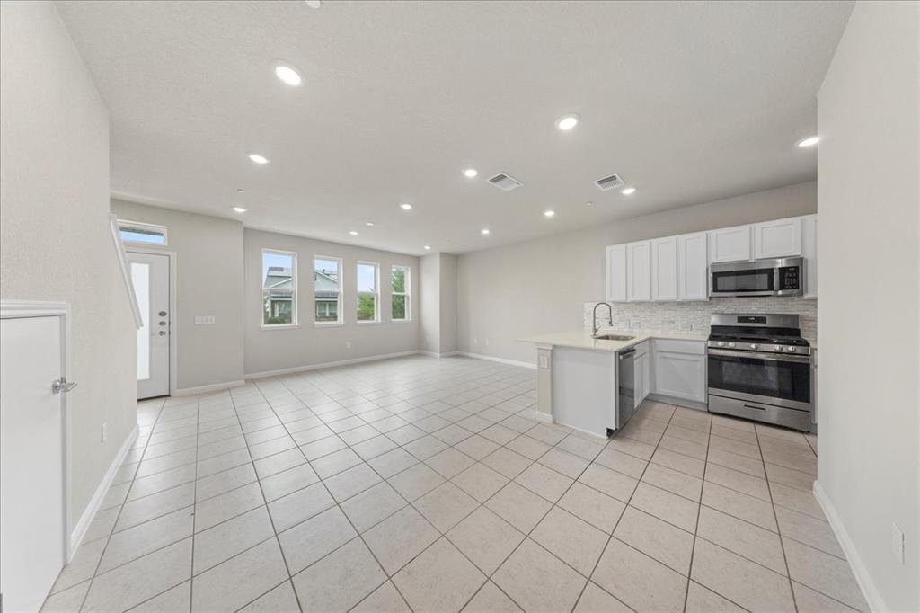9015 Cattle Baron Path, Unit 1502 Austin, TX 78747 - Photo 31 of 31 Kitchen with a peninsula, stainless steel appliances, open floor plan, decorative backsplash, and white cabinetry