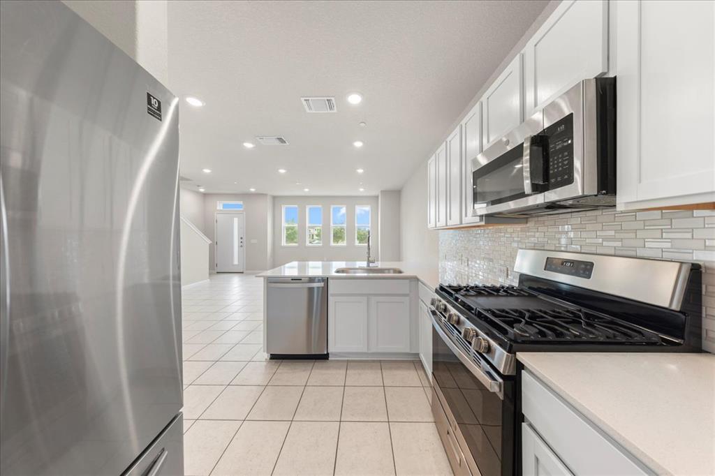 9015 Cattle Baron Path, Unit 1502 Austin, TX 78747 - Photo 5 of 31 Kitchen featuring stainless steel appliances, light tile patterned flooring, white cabinetry, a peninsula, and decorative backsplash