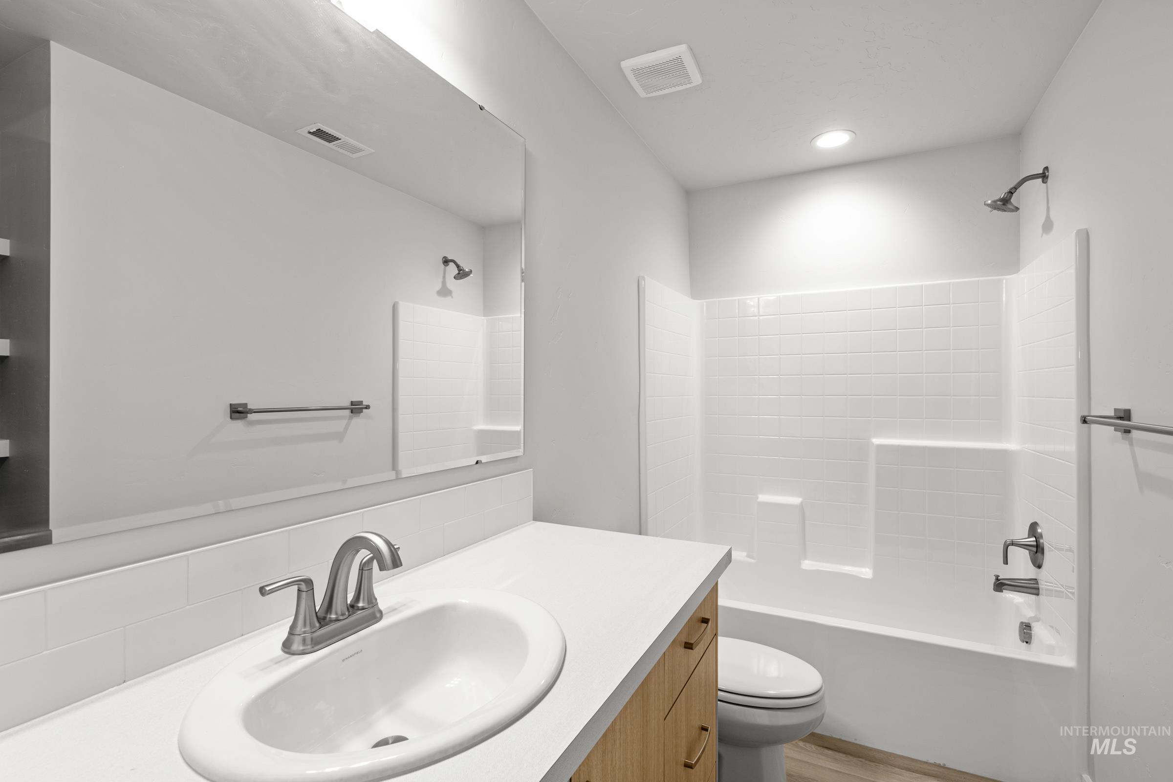 14056 Shiny Spruce Street Caldwell, ID 83607 - Photo 24 of 25 Contemporary bathroom featuring a wood-finish vanity with a white countertop and undermount sink, a large wall-mounted mirror, and a white tiled shower-tub combination