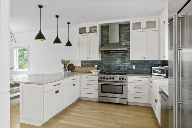 a kitchen with stainless steel appliances granite countertop a stove a sink and white cabinets with wooden floor