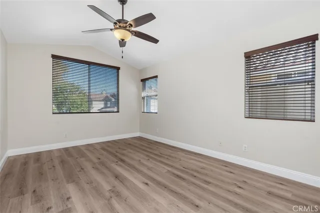 an empty room with wooden floor ceiling fan and windows