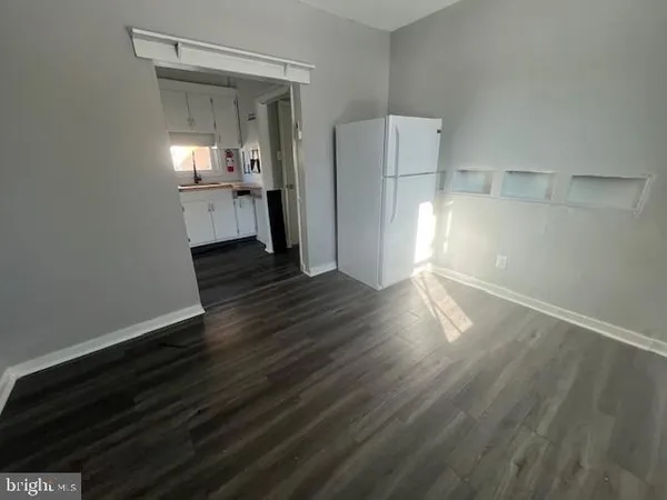 a view of empty room with wooden floor and kitchen
