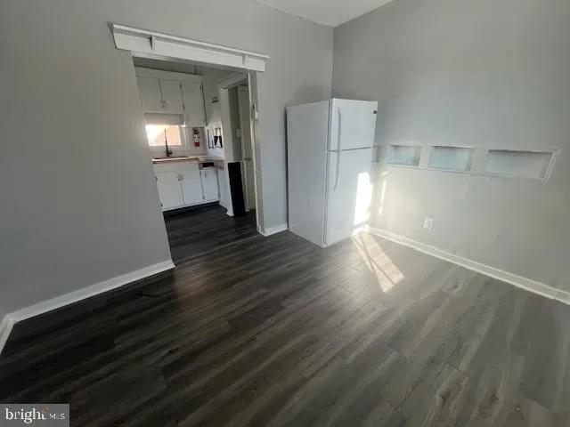 a view of empty room with wooden floor and kitchen