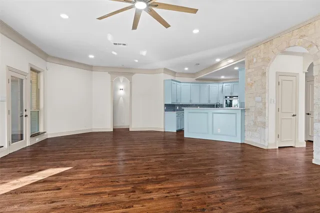 a view of an empty room with wooden floor and a kitchen