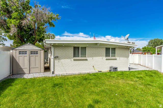 48 Moon Ridge Drive Murray, UT 84107 - Photo 23 of 30 Spacious rear yard featuring a green lawn, white vinyl fencing, concrete patio area, and an exterior storage shed