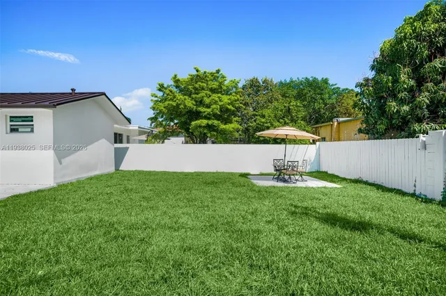 a view of a backyard with lawn chairs under an umbrella