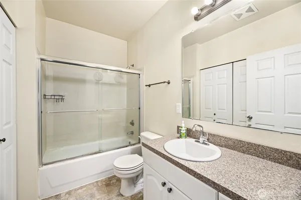 a bathroom with a granite countertop sink a toilet a mirror and shower
