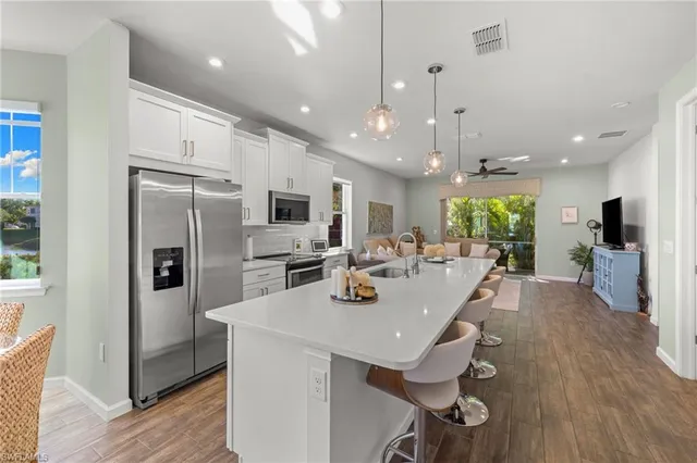 a kitchen with stainless steel appliances granite countertop a refrigerator a sink dishwasher a stove and white cabinets with wooden floor