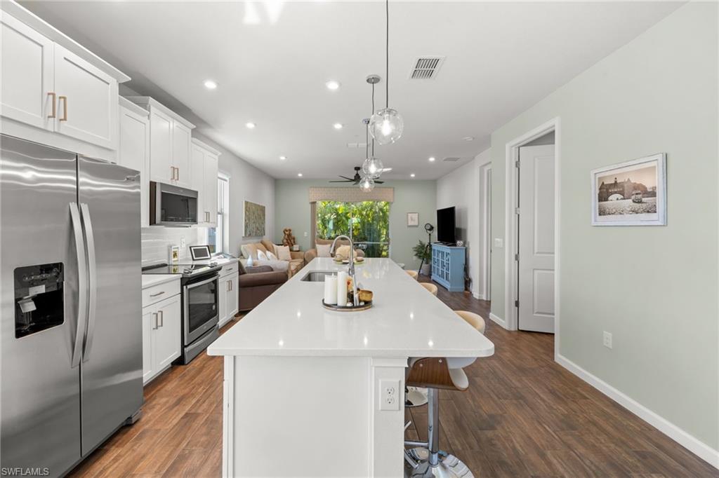 4619 Arboretum Circle, Unit 101 Naples, FL 34112 - Photo 8 of 41 a kitchen with a refrigerator a stove top oven a sink dishwasher a dining table and chairs with wooden floor