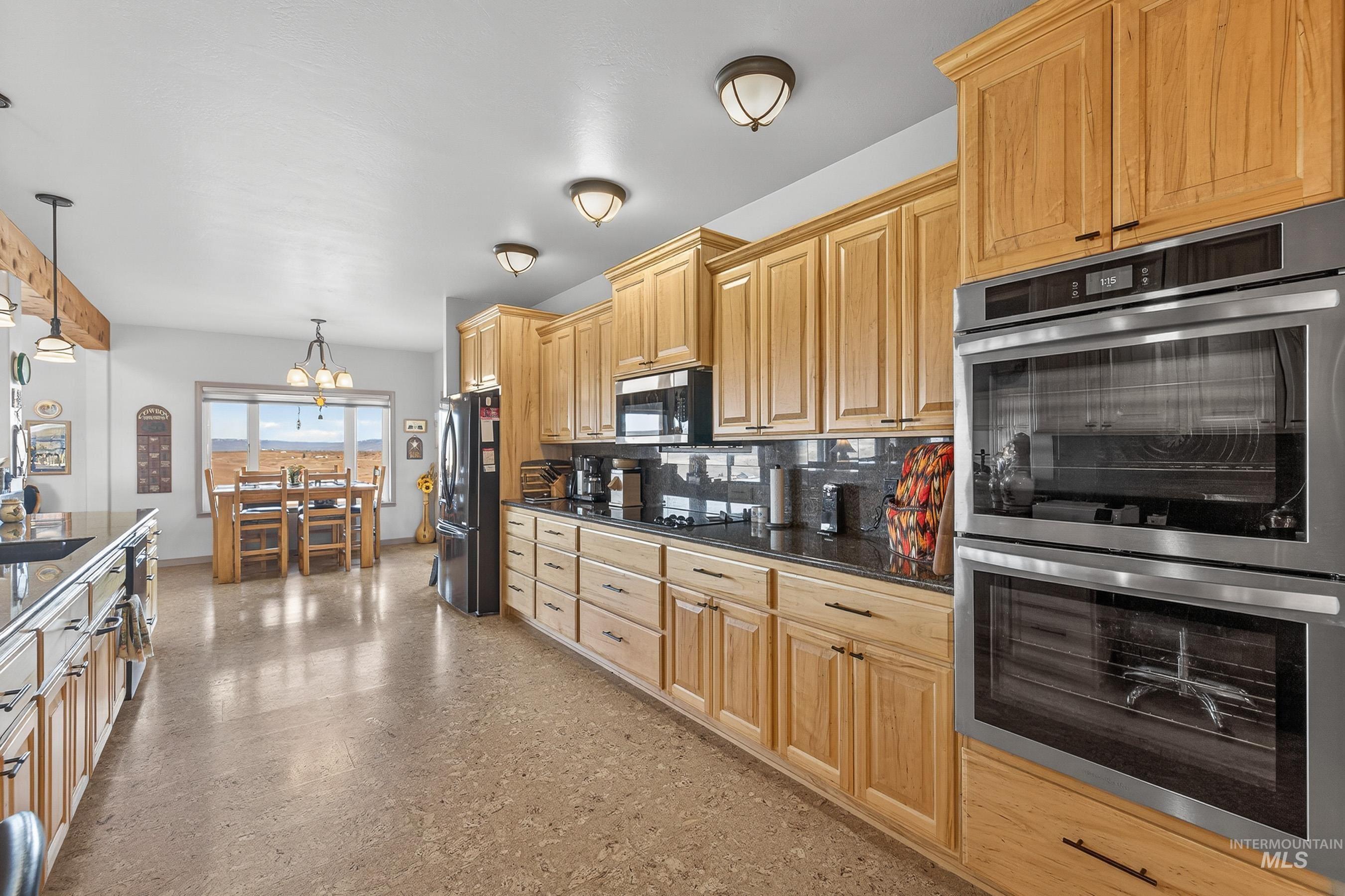 2195 Kilborn Lane Mesa, ID 83643 - Photo 7 of 50 Kitchen with appliances with stainless steel finishes, pendant lighting, decorative backsplash, dark stone countertops, and a chandelier