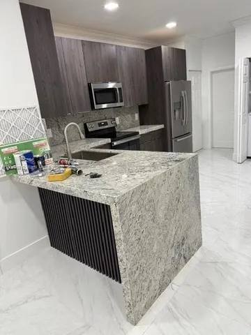 a kitchen with stainless steel appliances kitchen island granite countertop a refrigerator a stove a sink and a oven